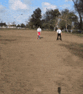 a man in a white shirt and red shorts is walking in a dirt field