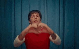 a young man in a red shirt is making a heart with his hands .