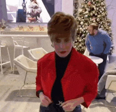 a woman in a red jacket is standing in front of a christmas tree ..