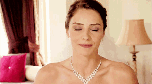 a bride with her eyes closed wearing a necklace and earrings