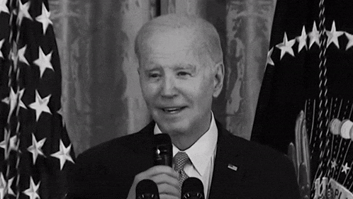 a man in a suit and tie is holding a microphone in front of a flag .
