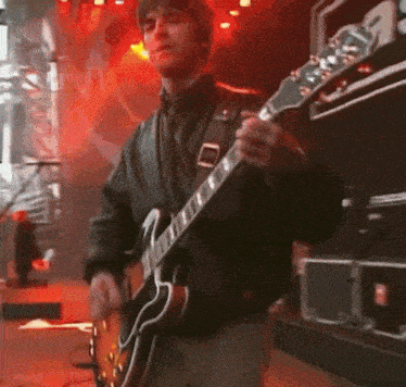 a man in a black jacket is playing an electric guitar