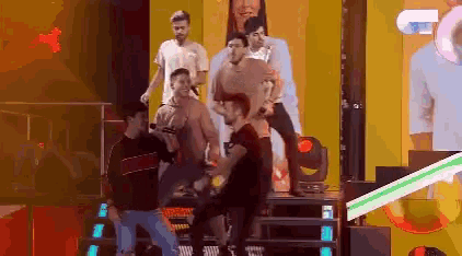a group of men are dancing on a stage in front of a large screen that says ' e ' on it