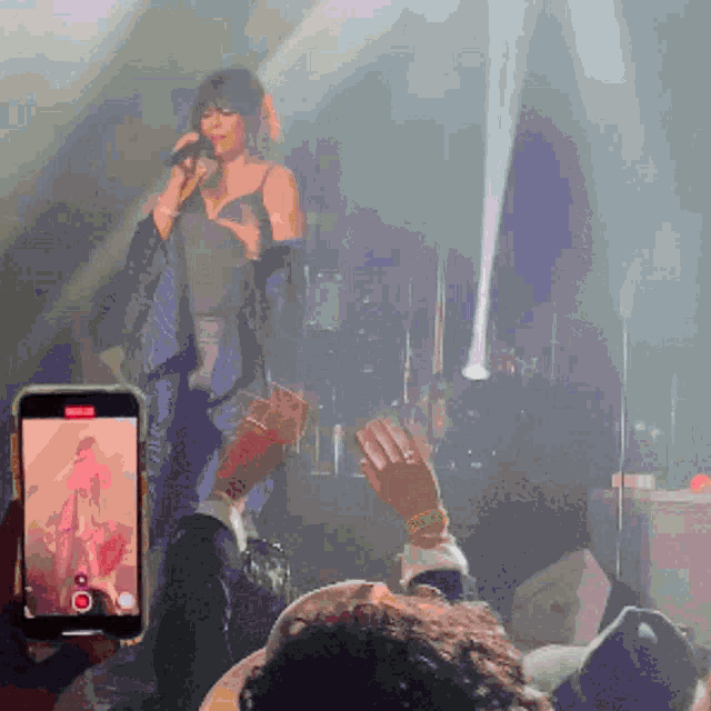 a woman singing into a microphone with a cell phone taking a picture