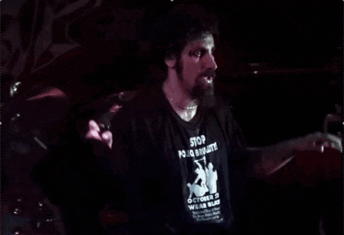 a man singing into a microphone in a dark room with a shirt that says ' nirvana ' on it