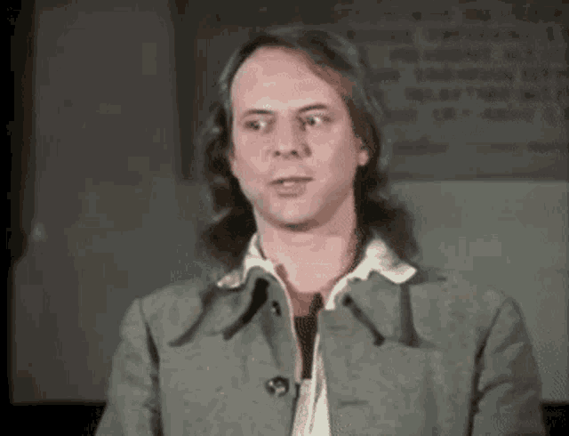 a man with long hair is wearing a grey coat
