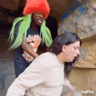 a man wearing a red hat and green hair is standing next to another man with long hair .