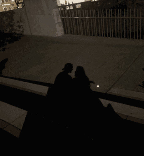a shadow of a couple kissing on a sidewalk at night