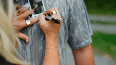 a woman is writing on a man 's shirt with a marker that says " i love you "