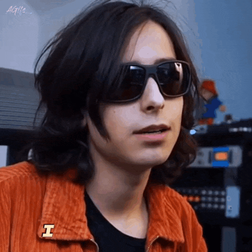 a man with long hair wearing sunglasses and an orange jacket
