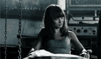 a woman in a gray tank top is chained to a chair