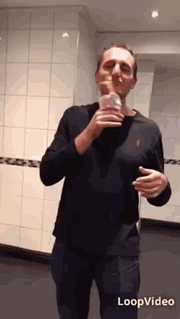 a man in a black shirt is eating an ice cream cone in a public restroom .