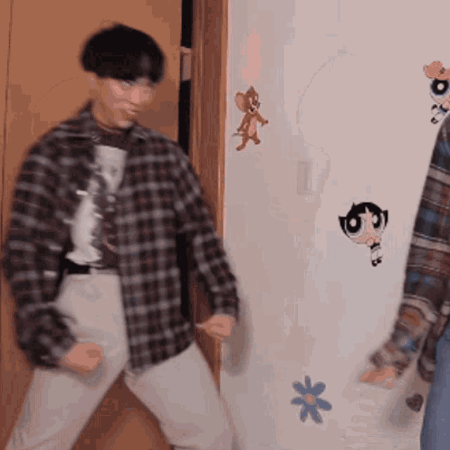 a man in a plaid shirt is dancing in front of a wall with powerpuff girls stickers on it .