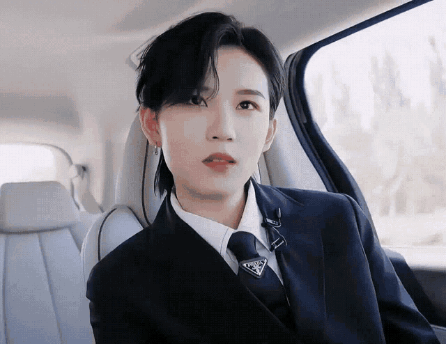 a woman in a suit and tie is sitting in the back seat of a car looking out the window
