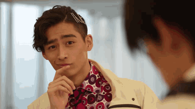 a man wearing a white jacket and a pink shirt with circles on it looks at himself in a mirror