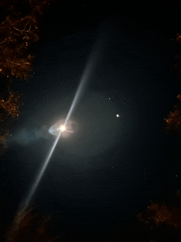 a bright light shines through a dark sky with trees in the foreground