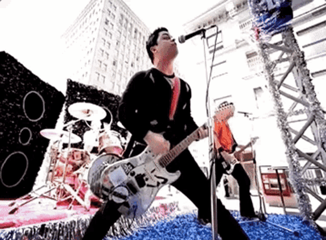 a man is playing a guitar and singing into a microphone while another man plays drums