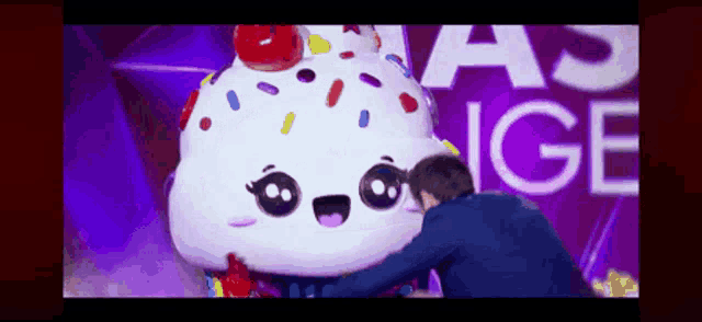 a man is hugging a cupcake with a cherry on top in front of a sign that says ice