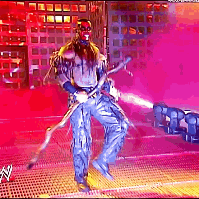 a wrestler is standing on a stage with a purple background and holding a spear .