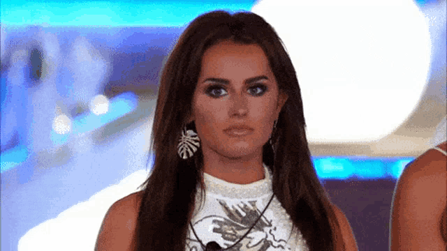 a woman with long hair is wearing earrings and a white top