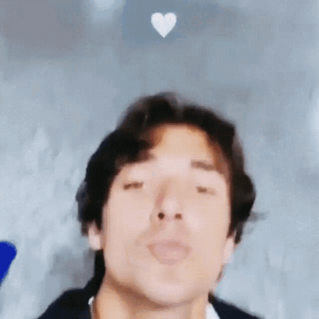 a close up of a man blowing a kiss with a heart behind him .