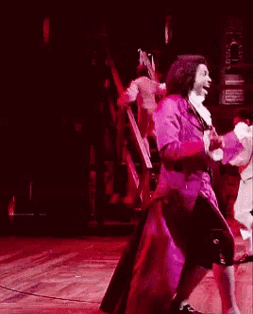 a man in a purple coat is dancing on a stage in front of a microphone .