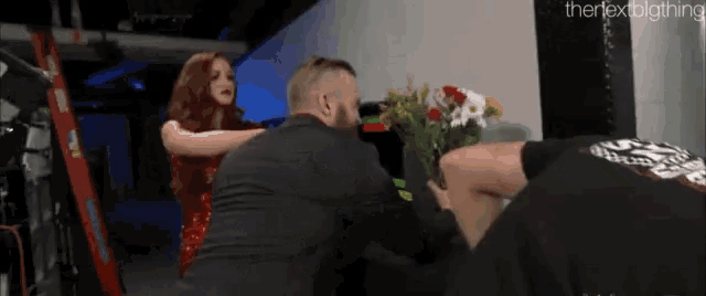 a man is holding a bouquet of flowers while a woman looks on .