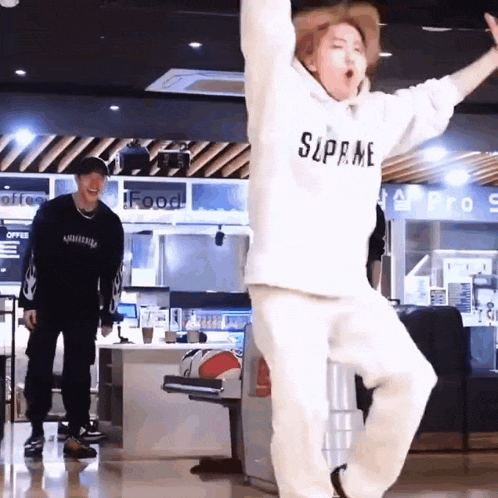 a man wearing a white supreme hoodie is dancing in a bowling alley .