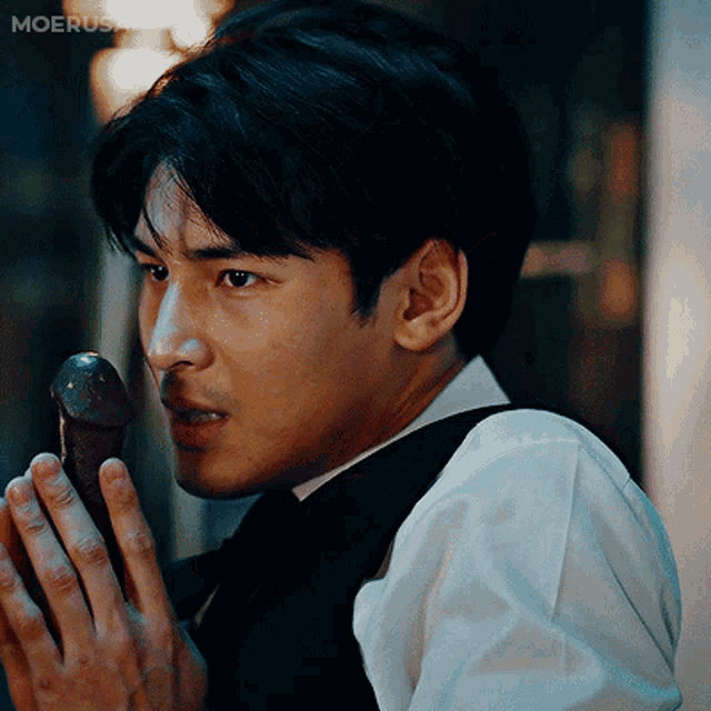 a man in a white shirt and black vest is holding a penis in his hand and the word moerusa is on the bottom