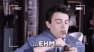 a young man is eating something with a spoon and the word ehm is written on the screen behind him .