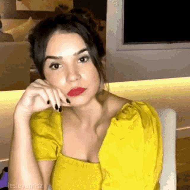 a woman wearing a yellow top and red lipstick is sitting in a chair .