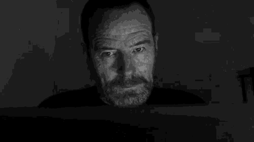 a man with a beard is looking at a computer screen in a dark room .
