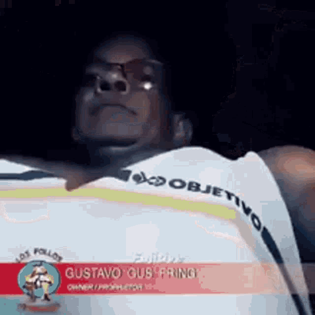 a man wearing a white shirt with the word objetivo on it is looking at the camera .