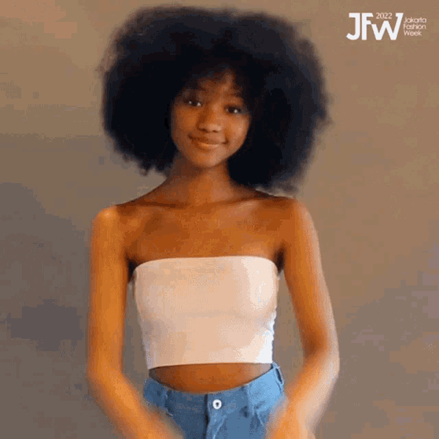 a woman wearing a white crop top and blue shorts is standing in front of a sign that says jfw 2022