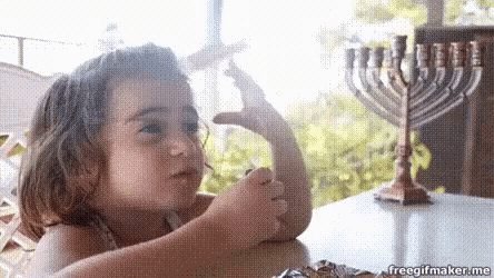 a little girl is sitting at a table with a menorah in the background eating candy .
