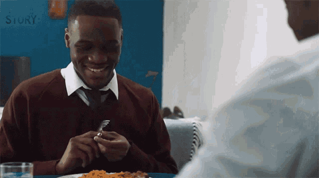a man sitting at a table with a plate of food in front of a blue wall that says blue story
