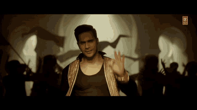 a man in a black shirt and gold jacket is waving his hand