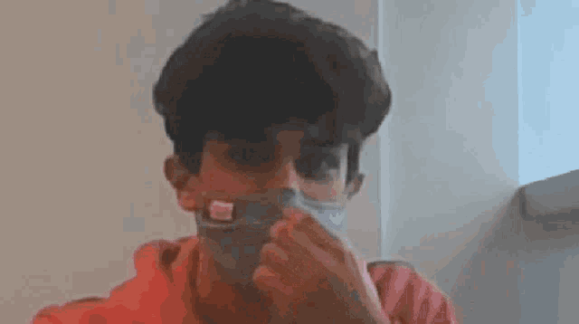a young boy wearing a face mask is brushing his teeth with a toothbrush .