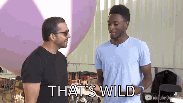 two men are standing next to each other in front of a balloon and one of them is saying that 's wild .