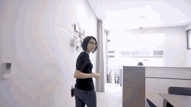 a woman wearing glasses and a black shirt stands in a room