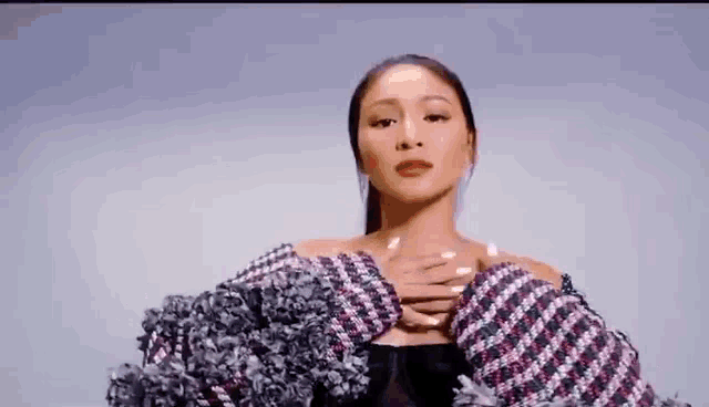 a woman is sitting down with her hands on her chest and wearing a plaid jacket .
