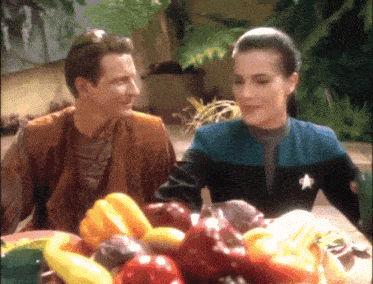 a man and a woman are sitting at a table with a bowl of fruit