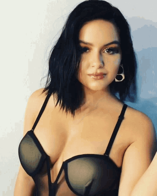 a woman in a black bra with a plunging neckline looks at the camera