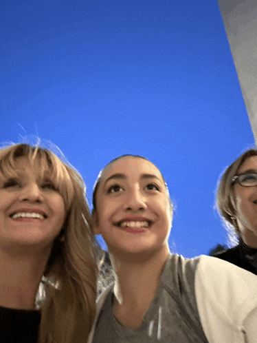 three women smile for a picture with a blue sky behind them