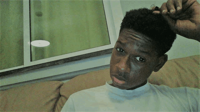 a young man is sitting on a couch and scratching his head