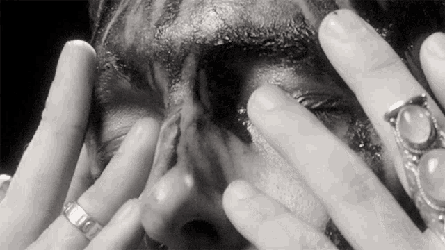 a close up of a person 's face with rings on their hands