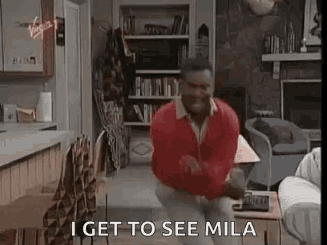 a man is dancing in a living room with the words `` i get to see mila '' written on the screen .