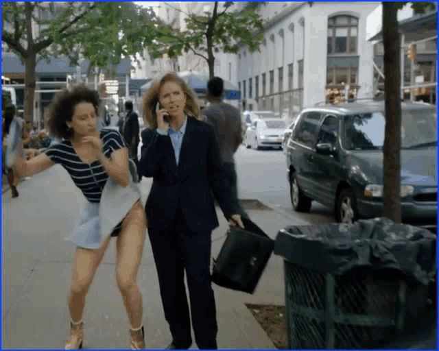 a woman in a suit is talking on a cell phone while a woman in shorts runs down the street