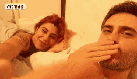 a man covering his mouth with his hand while a woman smiles in the background with the word mtmad on it