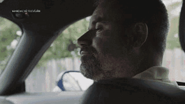 a man with a beard is sitting in the driver 's seat of a car with his eyes closed .